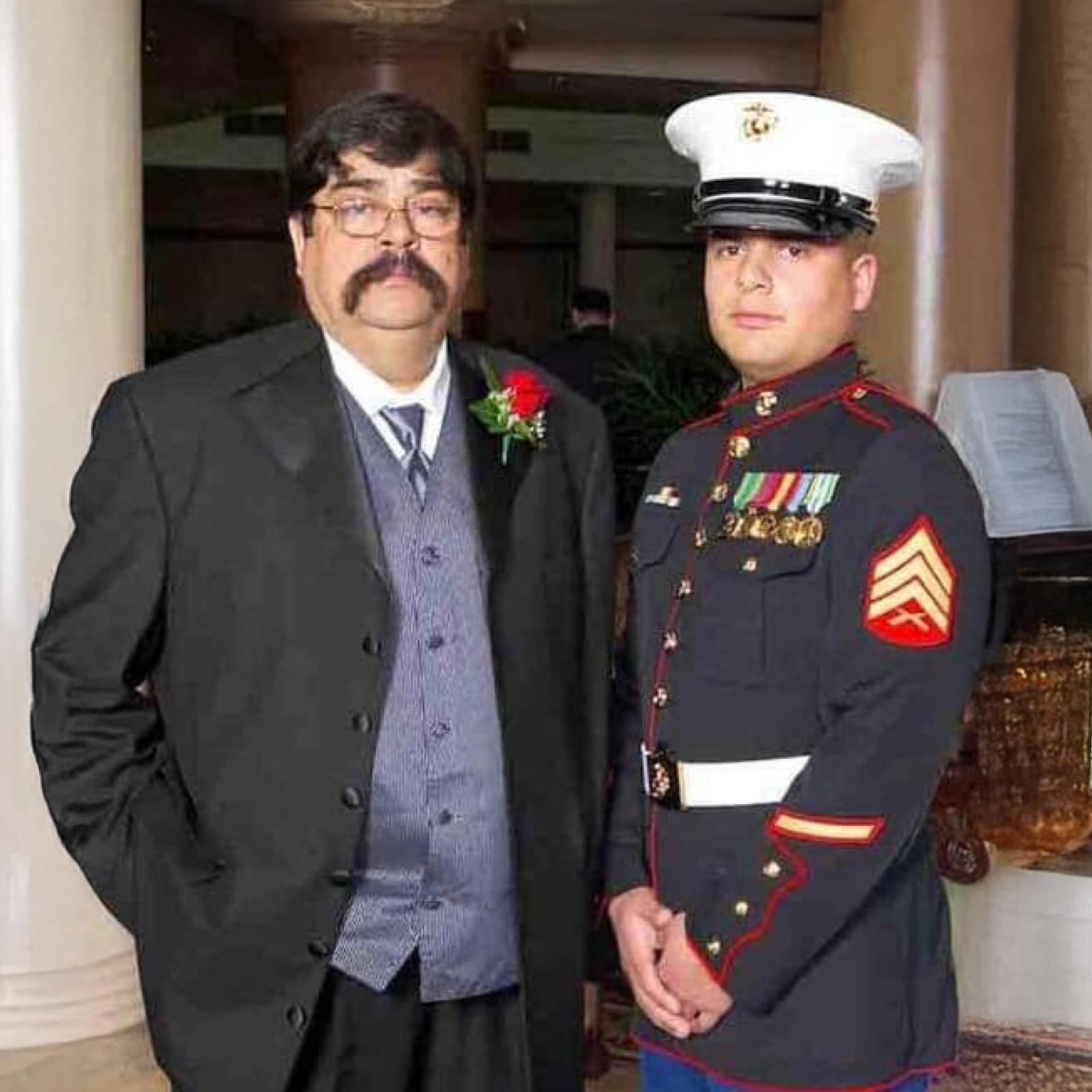 Luis Vindell standing beside his father, Fernando, both dressed formally and facing the camera.